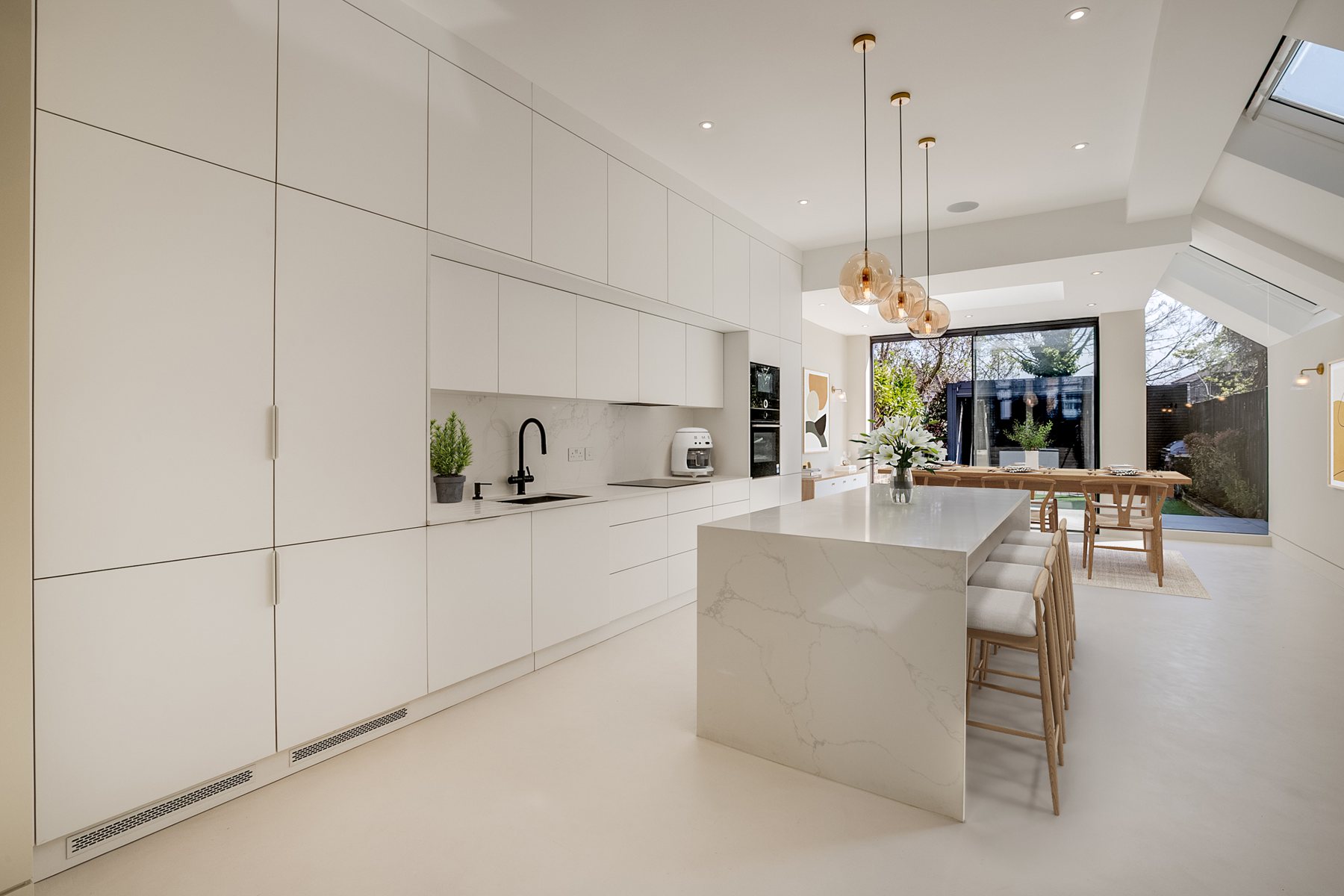 Long white kitchen leading to slim sliding doors and the garden